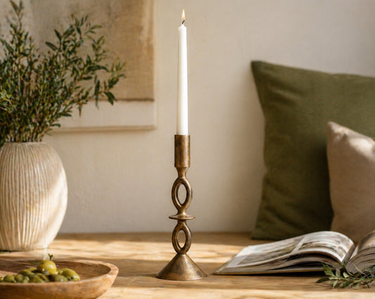 Candle in a brass holder on a wooden surface with a plant and open book in the background