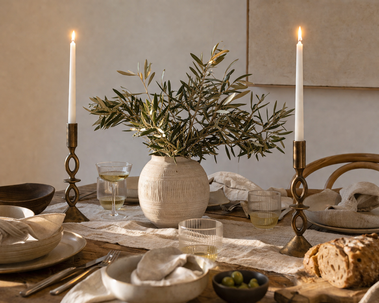 Dining table setting with gold candle holders, taper candles, vase, and bread on a neutral background from What a Host Home