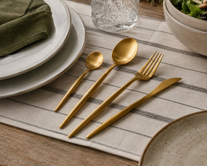 Gold cutlery set on a striped placemat with plates and a bowl in the background.