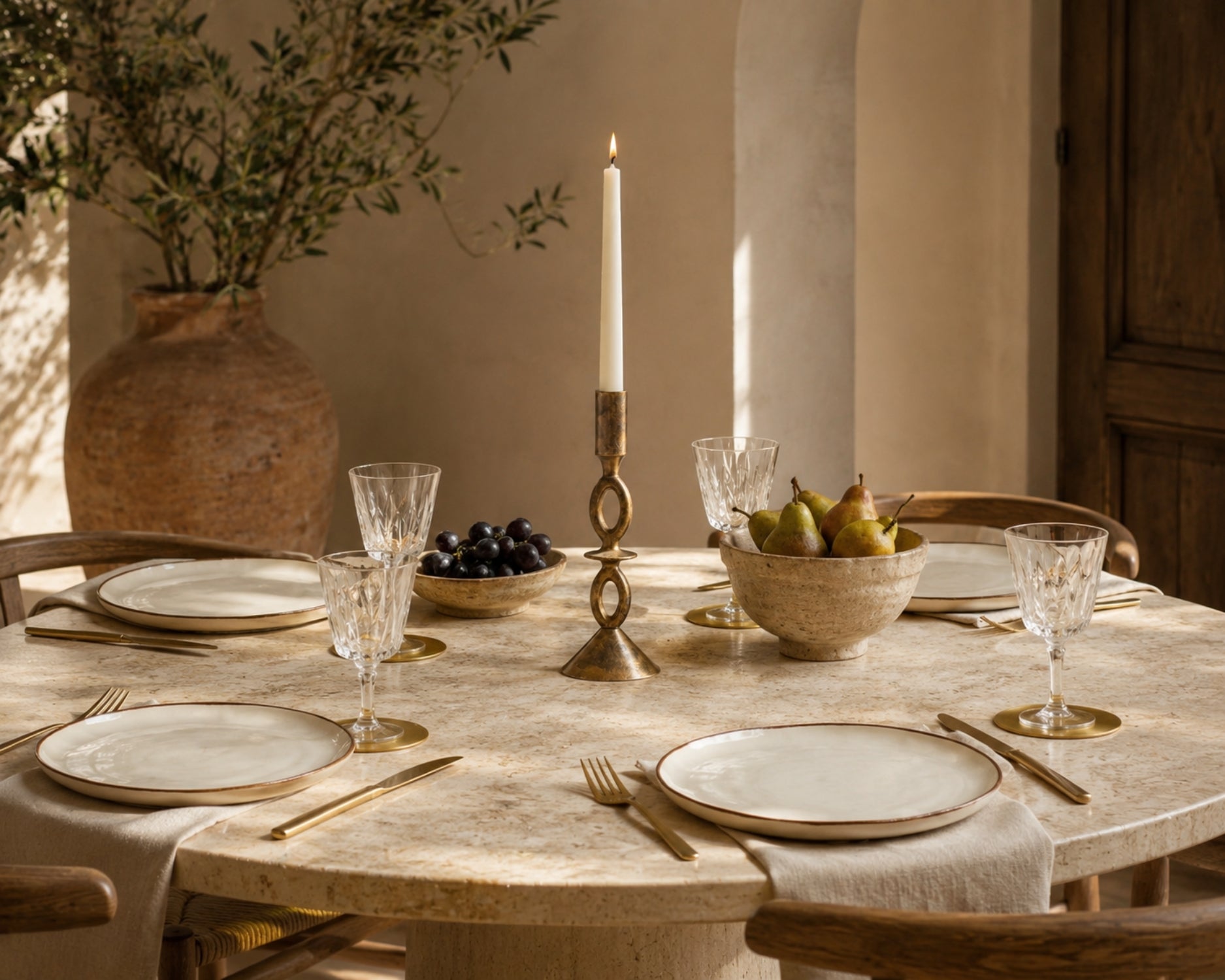 Dining table set with plates, glasses, and a candlestick holder in a warm-toned room.