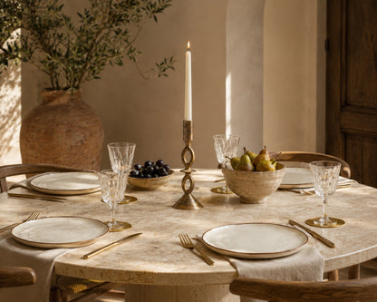Dining table set with plates, glasses, and a candlestick holder in a warm-toned room.